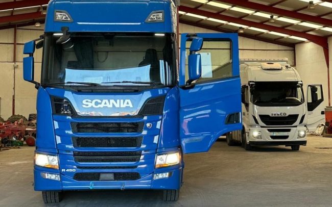 Camión azul Scania y camión blanco Iveco estacionados dentro de un almacén logístico.